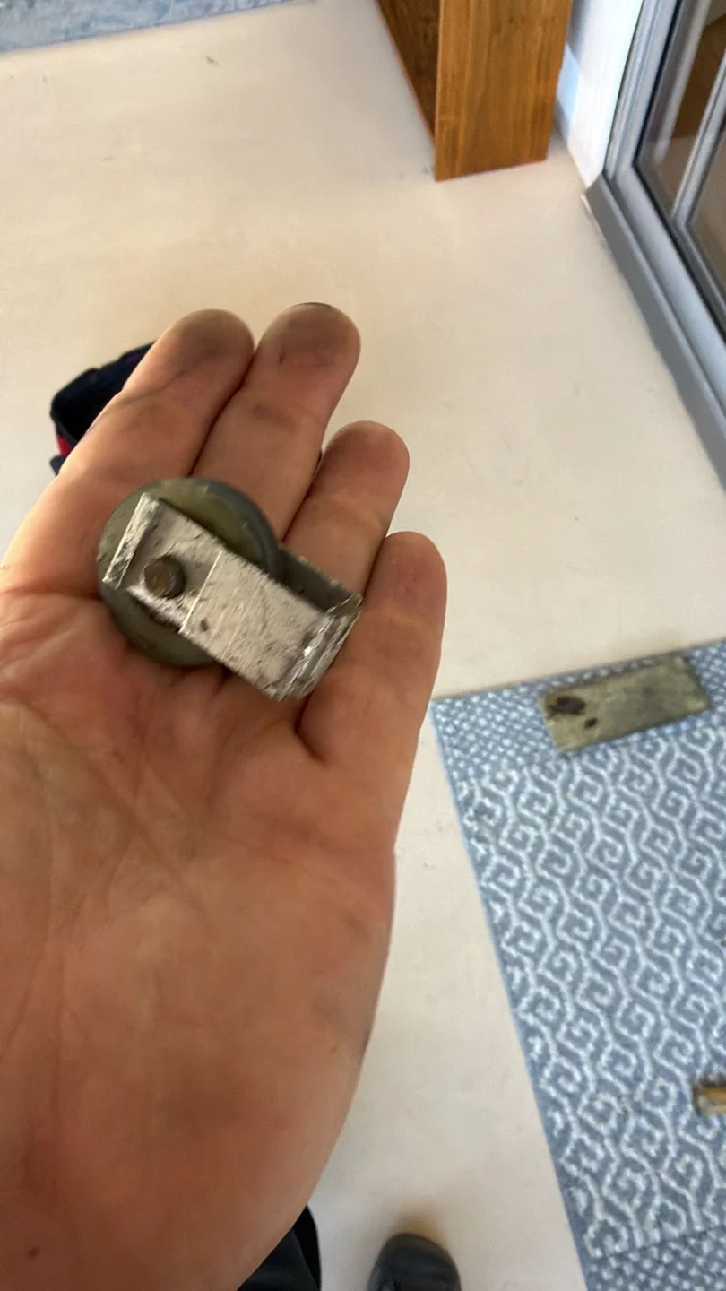 A removed metal door roller assembly held in a hand.