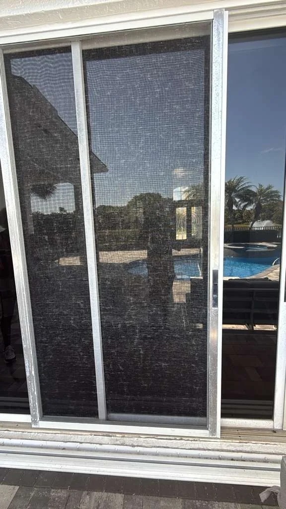 A screen panel beside white-framed sliding glass panels, viewed from outside.